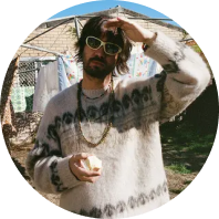 Picture of the artist Tame Impala standing in a backyard scratching his head.
